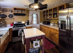 A kitchen with wooden cabinets, a stainless steel refrigerator, a stove, and a ceiling fan. - 3-bedroom farmhouse in charming Del Rio with with trout stream and 35 acres. (Del Rio)