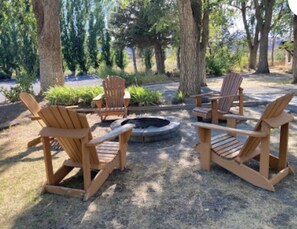 A circular seating area with wooden Adirondack chairs around a central fire pit.