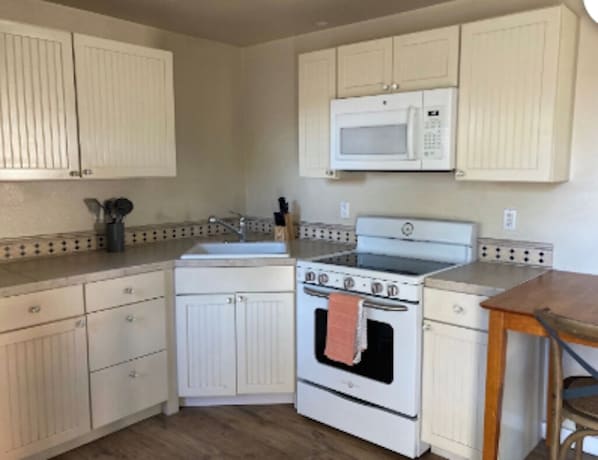 Una cocina con armarios blancos, estufa, microondas y una mesa de madera.