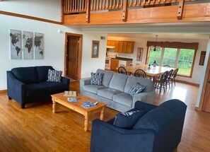 Un vaste espace de vie doté d’un haut plafond, d’un plancher en bois et d’un coin repas avec une grande table et des chaises.