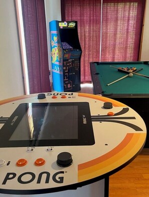 Ein Tischtennistisch mit digitaler Anzeigetafel, ein Billardtisch und eine farbenfrohe Spieluhr in einem Raum mit Vorhängen.