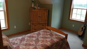 Ein Schlafzimmer mit einem Bett, einer Holzkommode, einem Fenster und einer Gitarre.