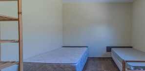 Ein kleiner, abgeschlossener Raum mit zwei Einzelbetten und einem Holzbett.