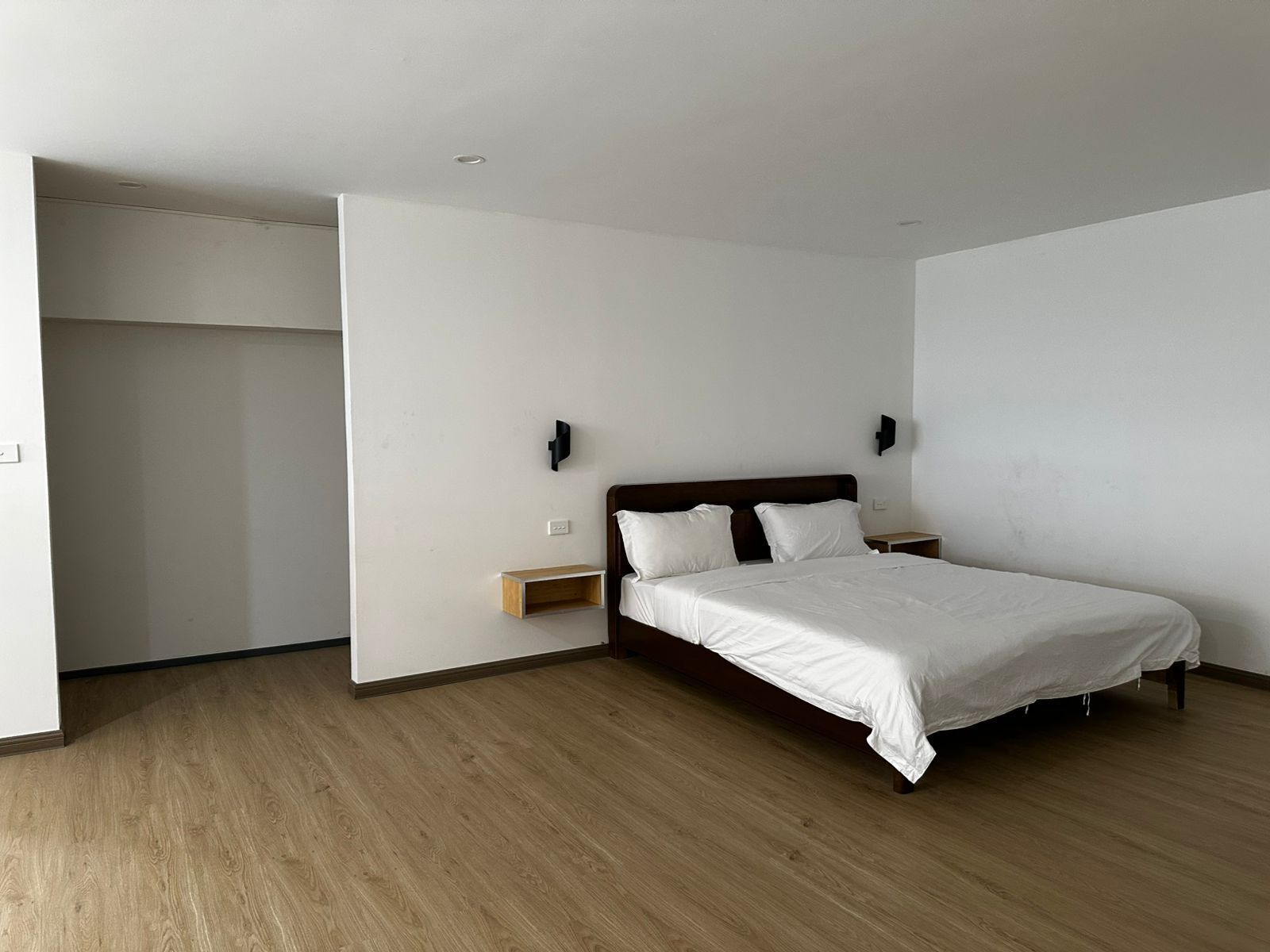 A bedroom with a bed, nightstands, a wooden floor, and a closet.