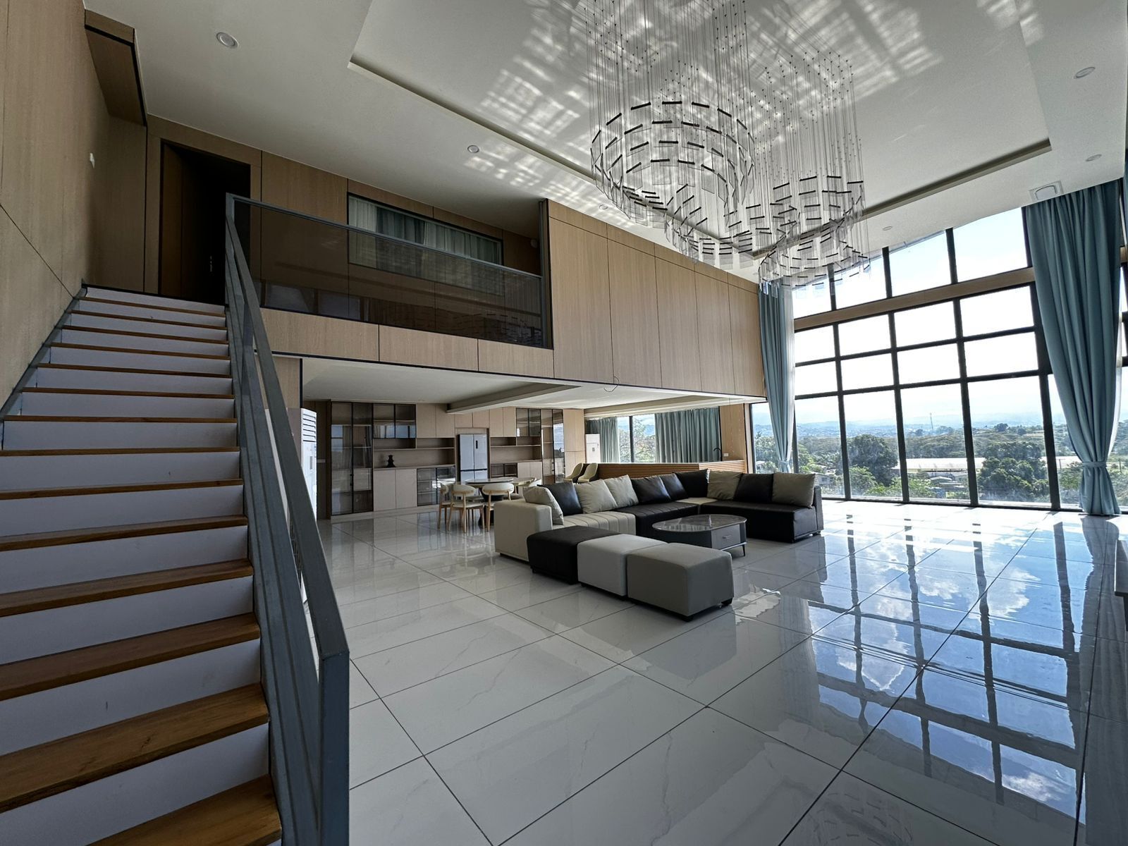 Un amplio espacio habitable con una escalera, un ventanal grande y una lámpara moderna.