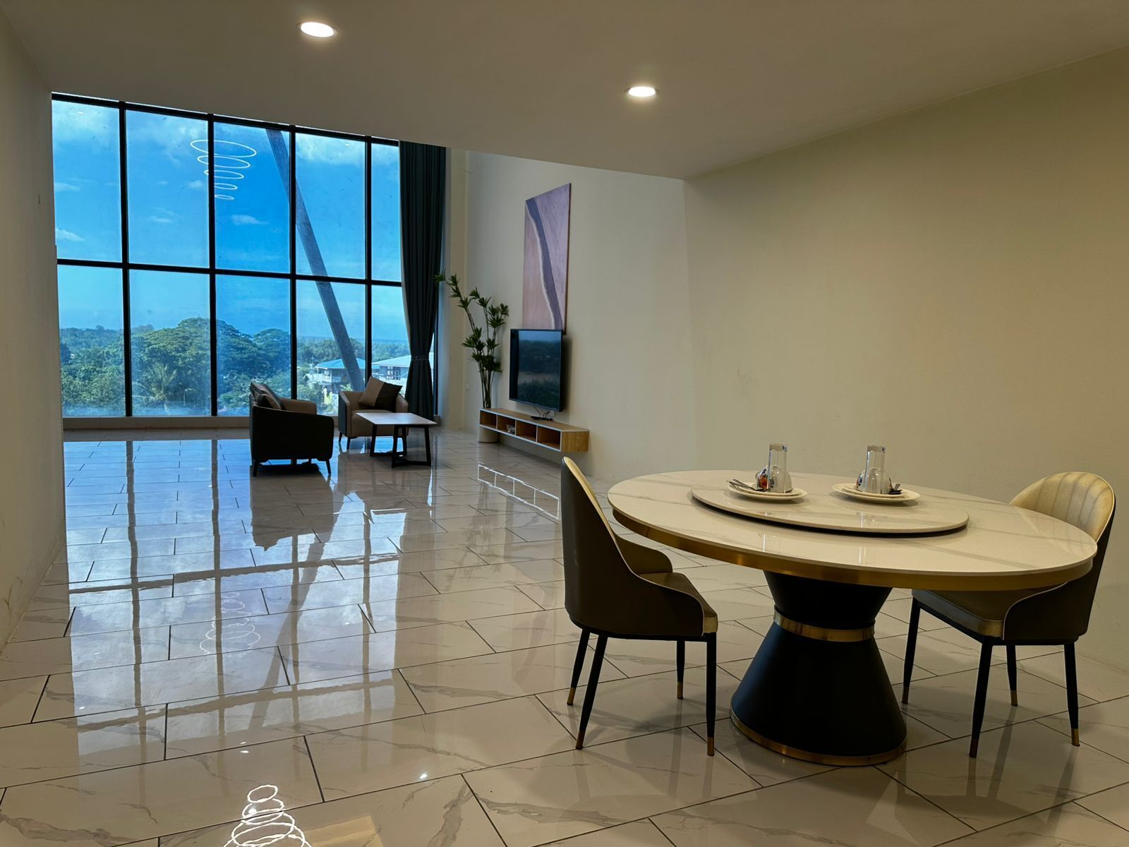 Un comedor moderno con una mesa redonda, sillas, un televisor y vistas al exterior.