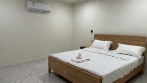 Una habitación de hotel con una cama de madera, ropa de cama blanca, un equipo de aire acondicionado blanco y suelo de baldosas de mármol.
