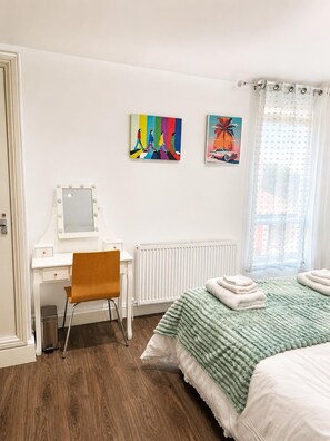 Ein Schlafzimmer mit einem Bett, einem Schreibtisch mit Spiegel, zwei Bildern und einer Heizung.