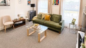 Een moderne woonkamer met een groene bank, een salontafel, een televisie en kunst aan de muren.
