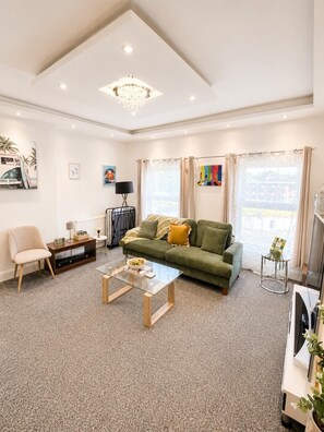 Ein modernes Wohnzimmer mit einem grünen Sofa, einem Couchtisch, einem Fernseher und Kunstwerken an den Wänden.