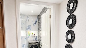 Een gang die leidt naar een wasserij, met een wasmachine, een deur en een muur met decoratieve ronde spiegels.