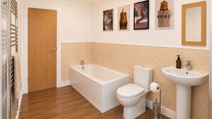 Une salle de bain avec une baignoire, des toilettes et un lavabo, un plancher en bois et une porte.