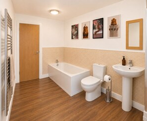 A bathroom with a bathtub, toilet, and sink, wooden flooring, and a door. - The Galleria Suite With Free Parking (Birmingham)