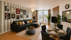Un salon moderne comprenant un canapé, une table basse, une table à manger et des chaises. Des tableaux encadrés ornent le mur, et un téléviseur est posé sur un meuble.