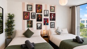 Une chambre d’hôtel avec deux lits, une grande fenêtre offrant une belle vue et un mur décoré de divers tableaux encadrés.
