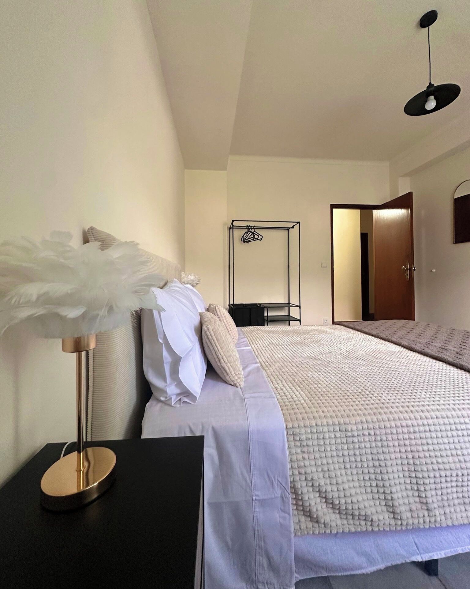 Quarto com cama, mesa de cabeceira, luminária, guarda-roupa e uma porta.