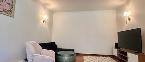 A living room with a sofa, ottoman, TV stand, and wall-mounted lights.