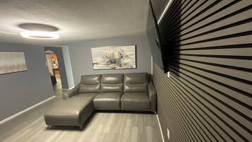 A modern living room with a sectional sofa, a flat-screen TV, and a ceiling light fixture.