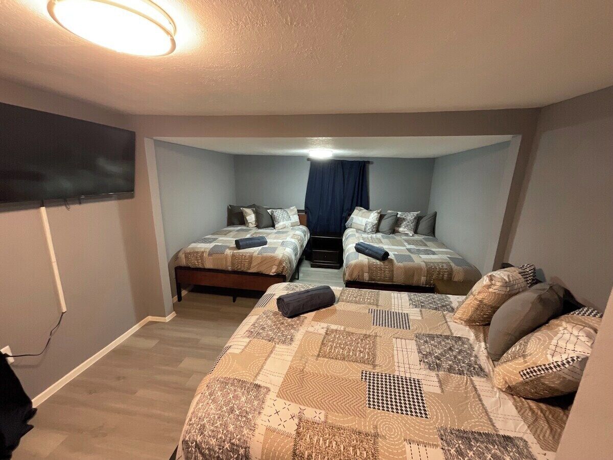 A bedroom with two beds, a TV mounted on the wall, and a staircase leading to an upper level.