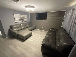 A living room with a gray sectional sofa, a flat-screen TV mounted on a slatted wall, and a ceiling light fixture. - Enjoyable 4-bedroom house with AC in charming Big Spring (Big Spring)