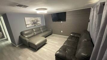 A living room with a sectional sofa, a flat-screen TV mounted on the wall, and a ceiling vent.