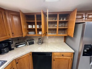 A compact kitchen with wooden cabinets, a built-in microwave, a coffee maker, and a dishwasher. - Enjoyable 4-bedroom house with AC in charming Big Spring (Big Spring)