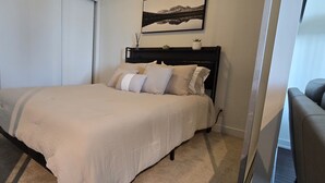 Une chambre à coucher avec un lit, une tête de lit, un tableau accroché au mur et une porte.