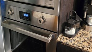 Une cuisine équipée d’un four et d’un micro-ondes encastrés, d’une machine à café et d’une horloge numérique.