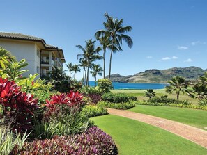 Un hotel con un césped cuidado, palmeras y vista al océano.
