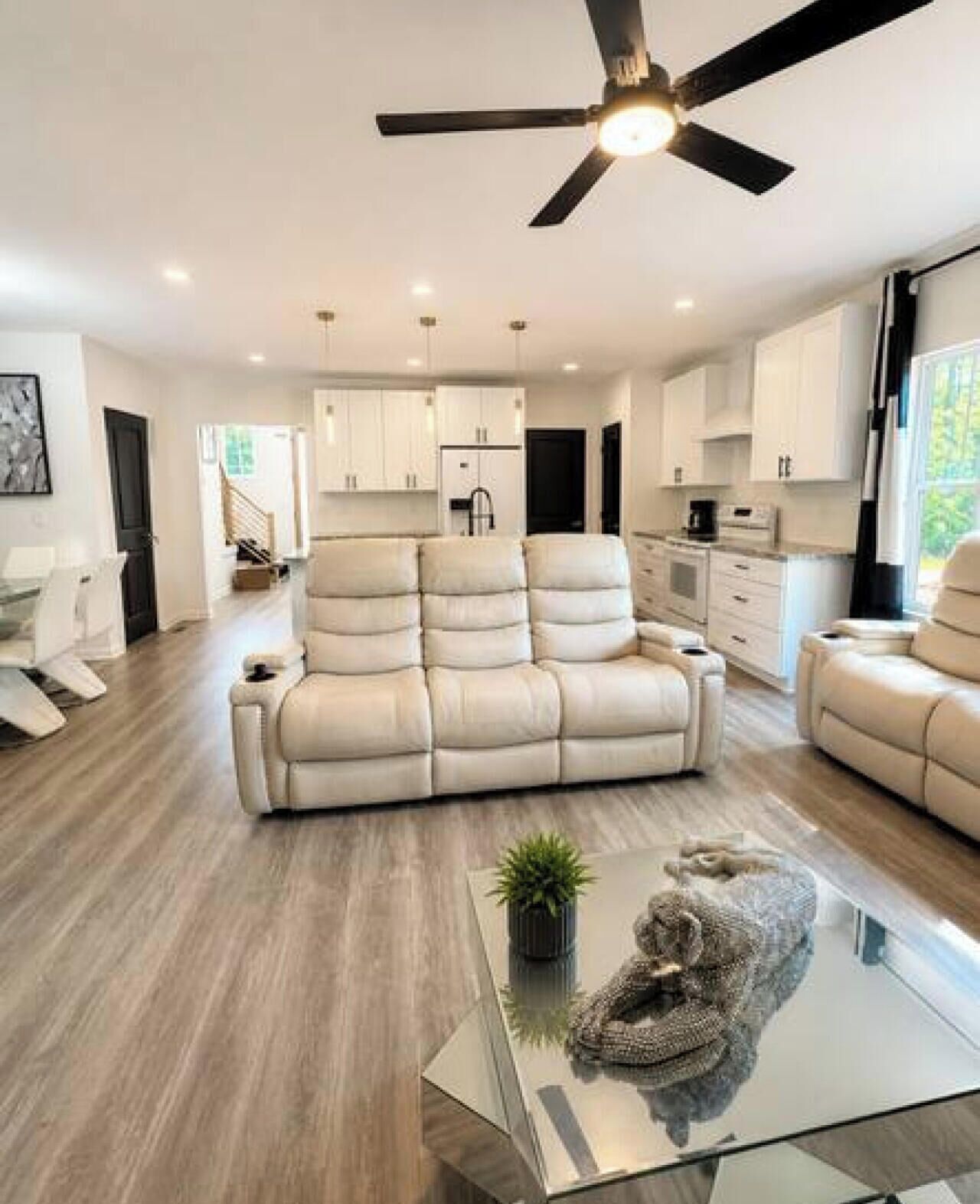 Ein großzügiger Wohnraum mit einem großen, beigefarbenen Sofa, einem Glastisch und einem Deckenventilator.