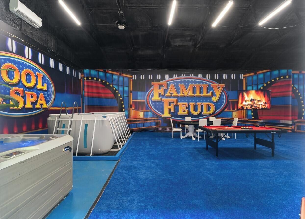 Ein Zimmer mit blauem Teppich, einem Billardtisch und einem Schild mit der Aufschrift 'Family Feud'.