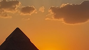 De silhouet van een piramide tegen een ondergaande zon.