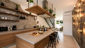 A modern kitchen with a brick backsplash, wooden shelves, and a central island with stools. - Lovely home in Zerava (Zerava)