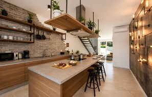 A modern kitchen with a brick backsplash, wooden shelves, and a central island with stools. - Lovely home in Zerava (Zerava)