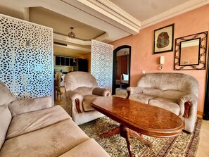 A living room with two beige armchairs, a wooden coffee table, decorative wall art, and a patterned rug. - Luxury Apartment - Pool & Ocean Right at Your Doorstep (IPTV, High-Speed Wi-Fi) (Tiguert)