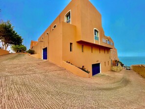 Ein Gebäude mit schrägem Dach, einer blauen Tür und Blick auf das Meer.