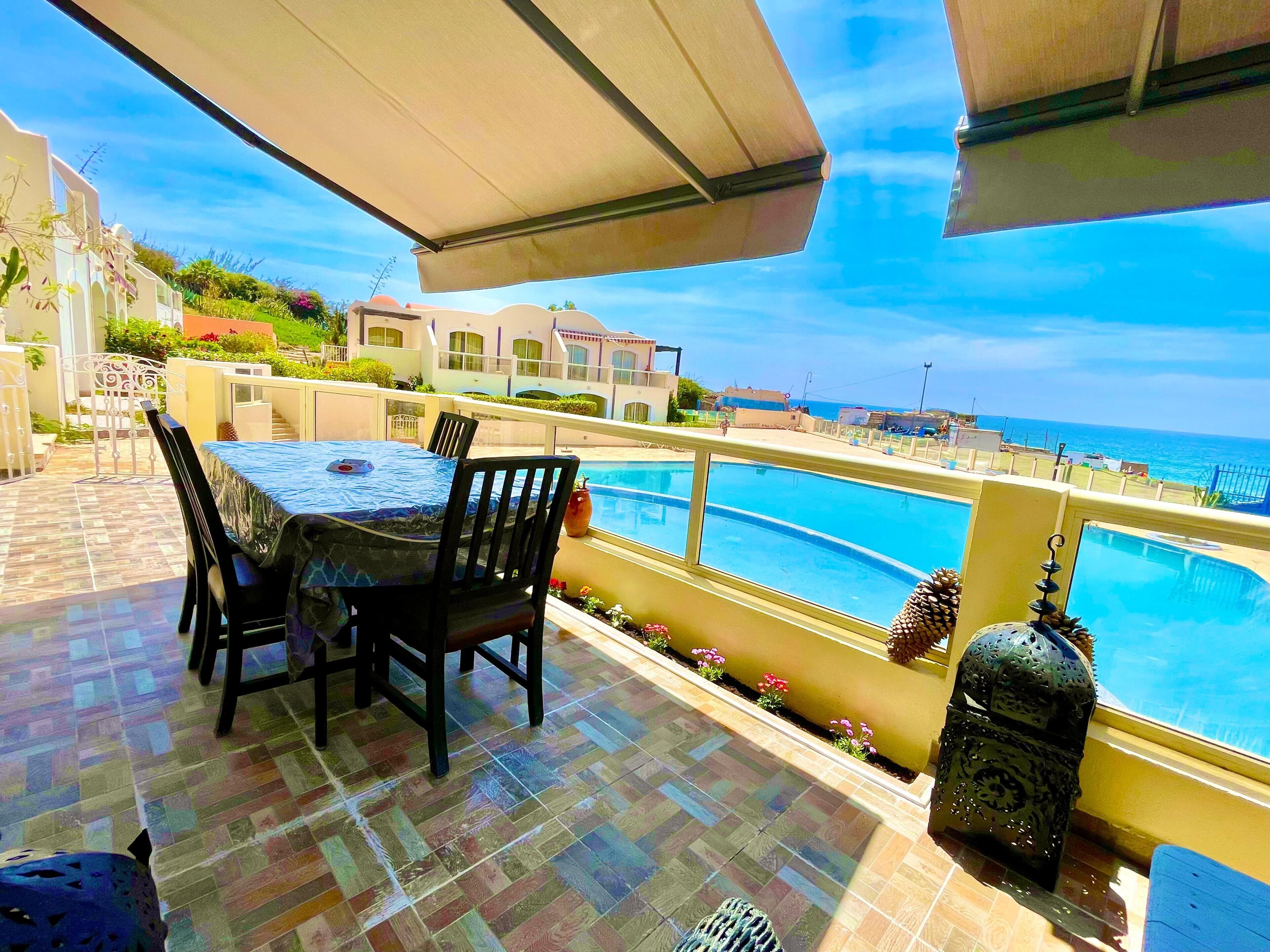 Une terrasse avec une table et des chaises, donnant sur une piscine et la mer.