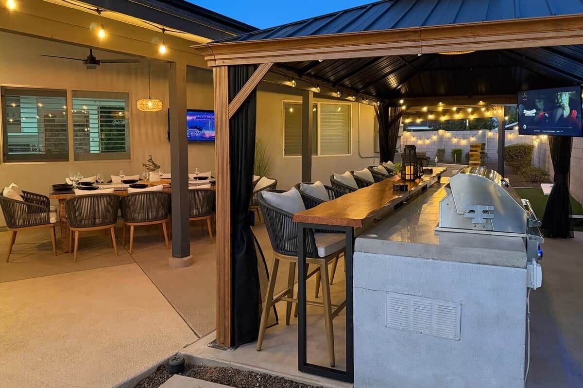 An outdoor bar area with seating, a grill, and a TV screen.