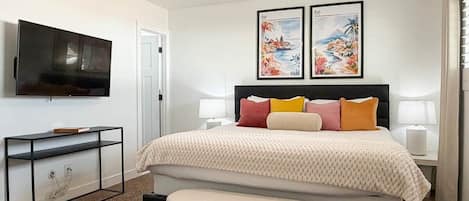 Un dormitorio con cama, televisor, ventilador de techo y dos cuadros en la pared.