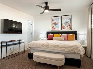 A bedroom with a bed, a TV, a ceiling fan, and two framed pictures on the wall. - Pool, Putts & Paradise | Modern Lux Golden Getaway (Scottsdale)