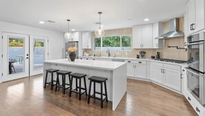 A modern kitchen with a large island, bar stools, stainless steel appliances, and a view of the outdoors. - Pool, Putts & Paradise | Modern Lux Golden Getaway (Scottsdale)
