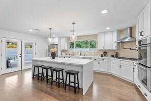 A modern kitchen with a large island, bar stools, stainless steel appliances, and a view of the outdoors. - Pool, Putts & Paradise | Modern Lux Golden Getaway (Scottsdale)
