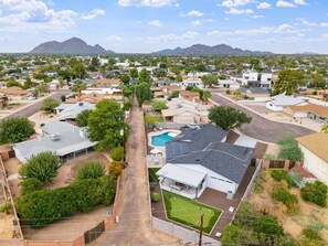 A residential area with houses, a swimming pool, and a mountain in the background. - Pool, Putts & Paradise | Modern Lux Golden Getaway (Scottsdale)