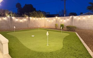 A miniature golf course with a brick wall and string lights. - Pool, Putts & Paradise | Modern Lux Golden Getaway (Scottsdale)