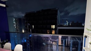 Een balkon met uitzicht op een stadsbeeld in de nacht, een tafel met een roze tafelkleed en een stoel.
