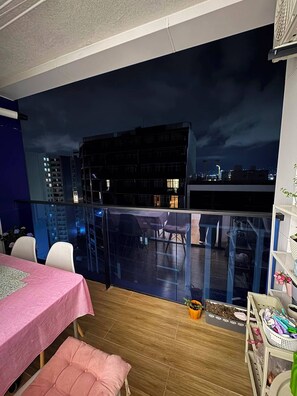 Ein Balkon mit Blick auf eine nächtliche Skyline, ein Tisch mit rosa Tischdecke und ein Stuhl.