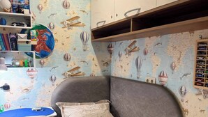 Een kinderkamer met een bed, bureau en planken vol speelgoed.