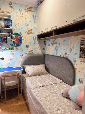 Ein Kinderzimmer mit einem Bett, einem Schreibtisch und Regalen voller Spielzeug.