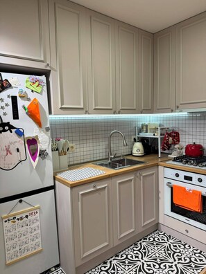 Eine Küche mit weißen Schränken, einer gefliesten Spritzschutzwand, einem Spülbecken, einem Herd und einem Kühlschrank mit Magneten und Notizen.
