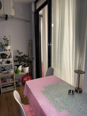 A room with a bed, a small table, a chair, a shelf with plants, and a window with curtains. - Fabulous 2-bedroom apartment with AC in vibrant Batumi (Batumi)